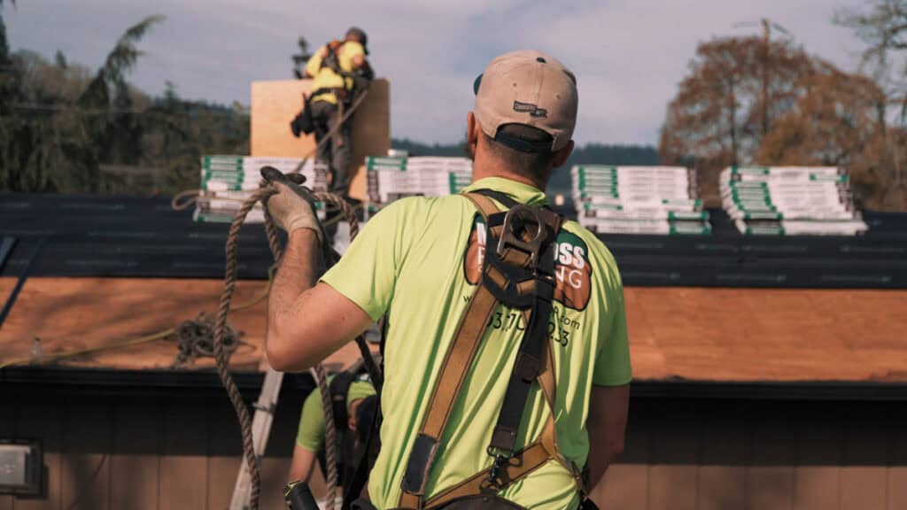 Roofers installing a new roof in Oregon using safety harness and fall protection equipment