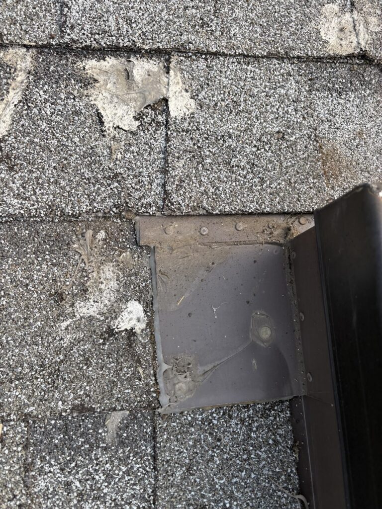 Metal skylight flashing beside weathered asphalt shingles and existing sealant