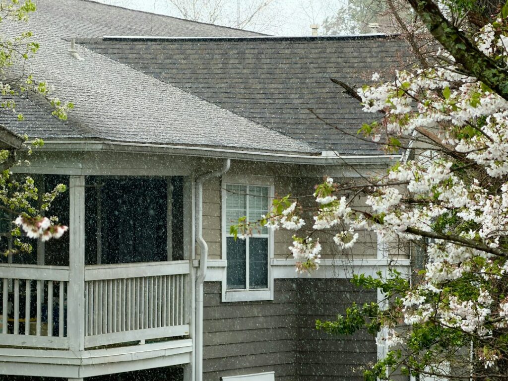 Rain falling from the roof edge of a house surrounded by trees.